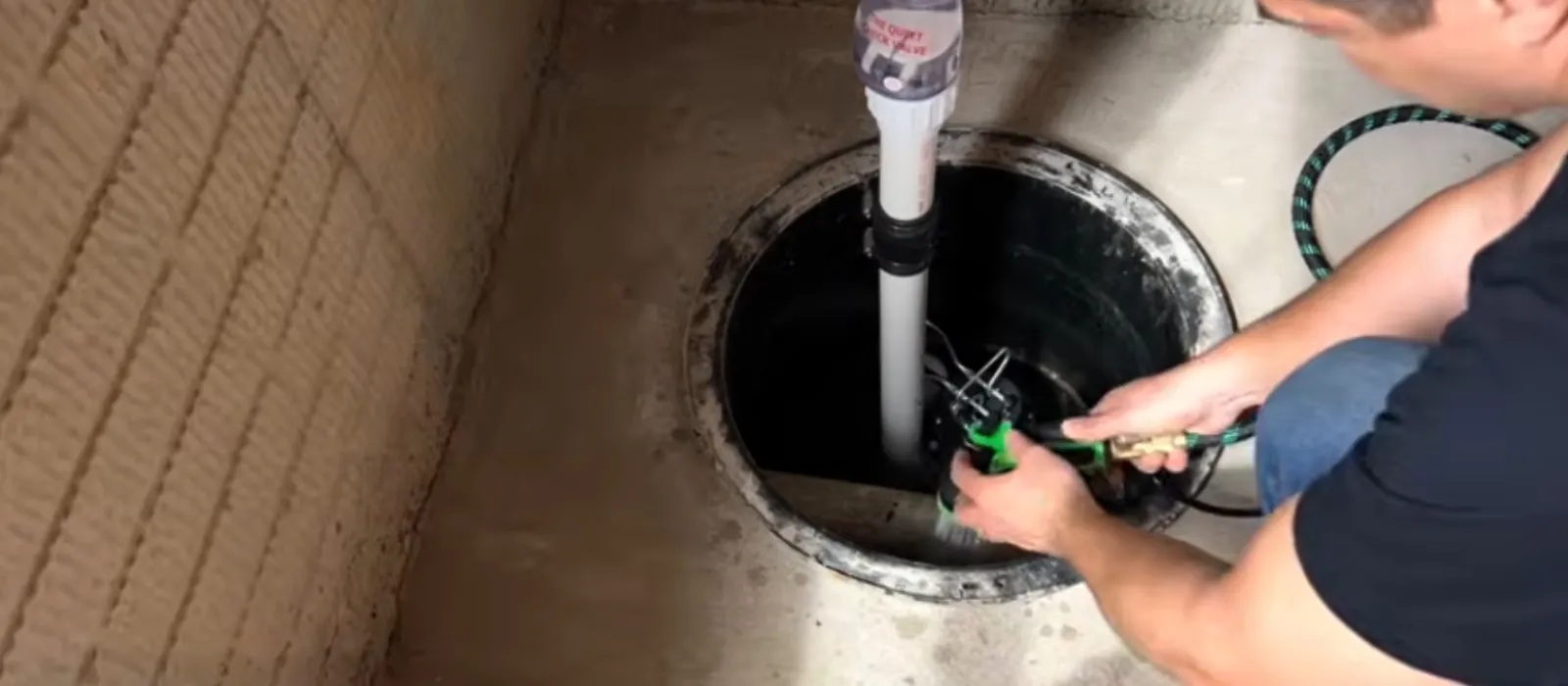 Person fitting a sump pump and PVC discharge pipe in a basement pit