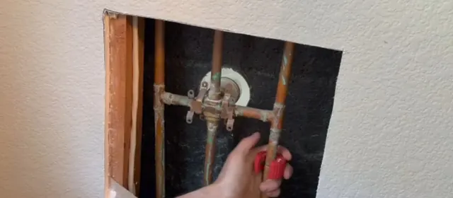 Hand reaching a shower valve through an open access panel in a bathroom wall