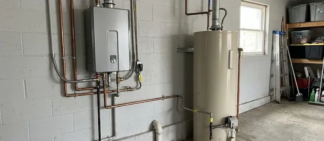 Wall mounted tankless water heater beside a traditional tank water heater in a garage
